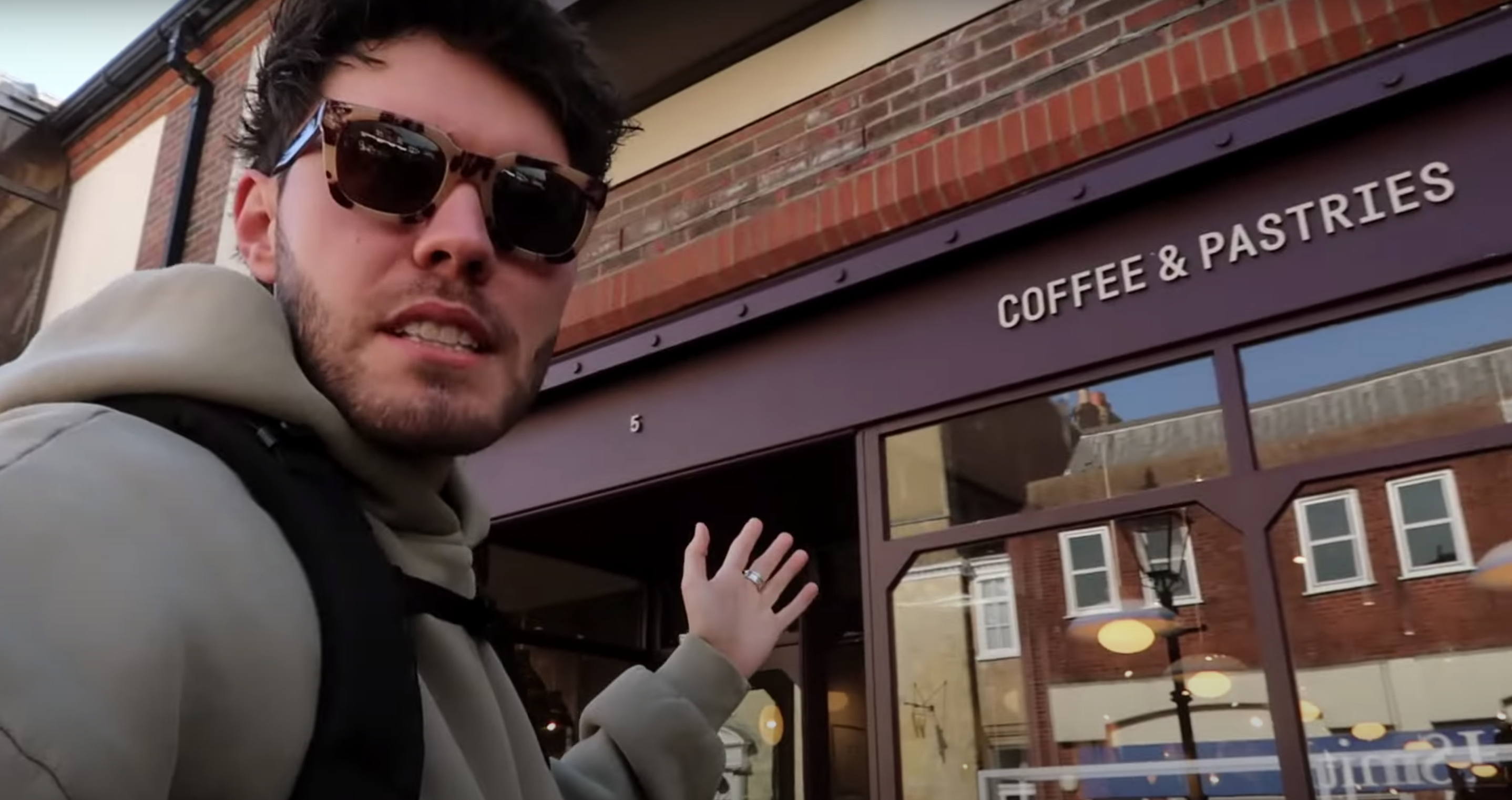 Alfie Deyes standing outside Coffee & Pastries in Lewes, pointing at the bakery sign with a smile.