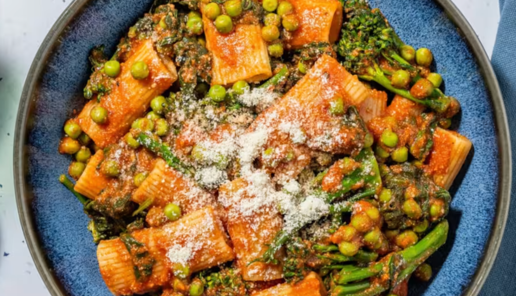 Close-up of a plate of HelloFresh Cajun-Spiced Tomato & Super Greens Rigatoni, garnished with Parmesan cheese and served on a stylish blue plate.