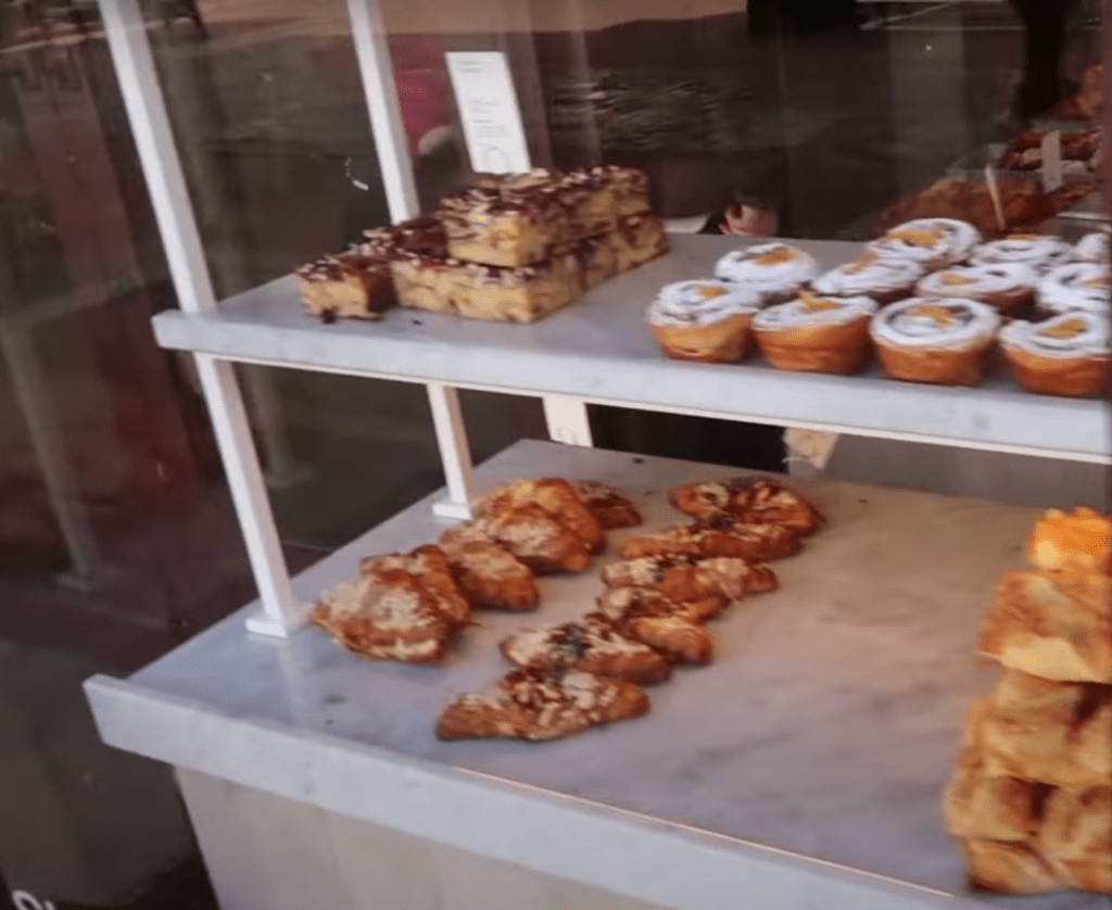 A bakery window display showing an assortment of pastries, including fruit-filled danishes, crumble slices, and freshly baked croissants.