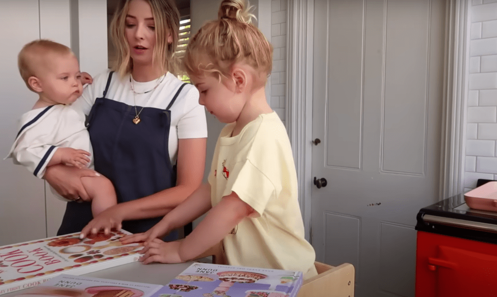 oe Sugg holds Novie while Ottilie browses through cookbooks, choosing a baking recipe.