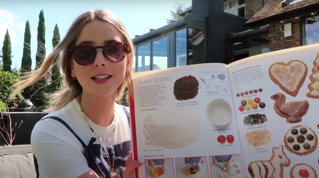 Zoe Sugg holds open a cookbook featuring an easy icing recipe and decorated biscuits.